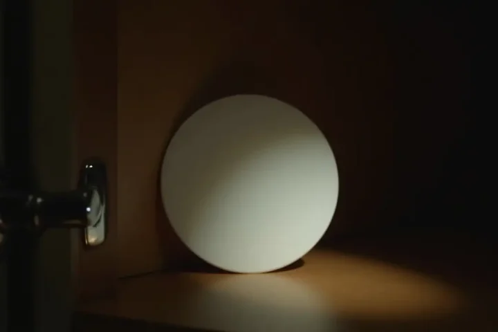 Dark inside corner of a kitchen cabinet with a small plain white bait disc against the back edge